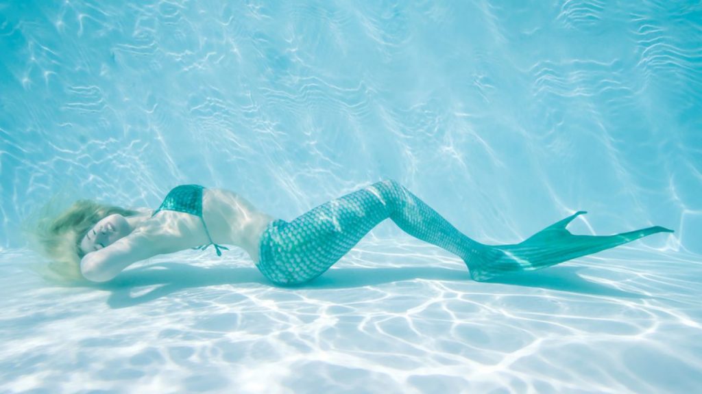 sereia de calda azul deitada no fundo da piscina