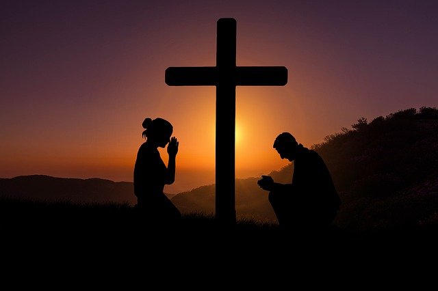 homem e mulher orando diante da cruz